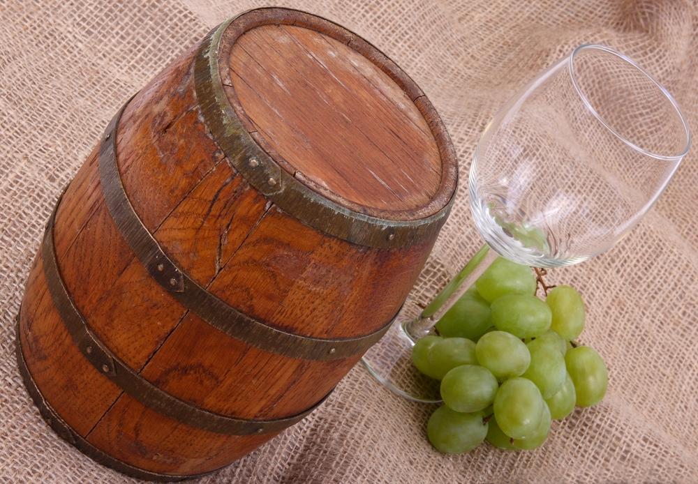 Kleines Weinfass als Deko neben einem Weinglas und Weintrauben
